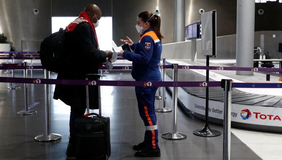 Un miembro de la Defensa Civil francesa verifica los documentos de un viajero en el aeropuerto de París-Charles de Gaulle en Roissy, al norte de París, el 5 de febrero de 2021. (GONZALO FUENTES / POOL / AFP).