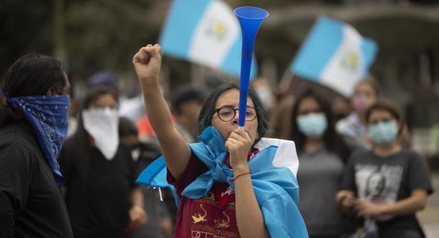 Una mujer levanta el puño y hace sonar un cuerno durante una protesta frente al Palacio Nacional, un día después de que los manifestantes prendieran fuego a una parte del edificio del Congreso, en la Ciudad de Guatemala. (AP / Moises Castillo)