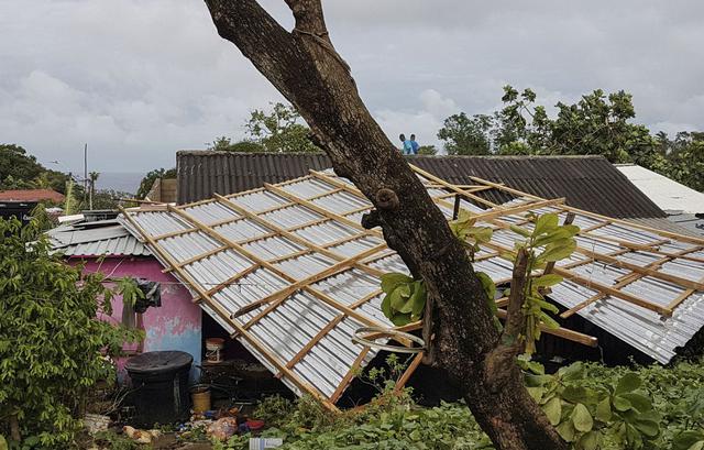 La gente se para en el techo de una casa parcialmente destruida tras el paso del huracán Iota en San Andrés. (Foto de LIANA FLOREZ / AFP).
