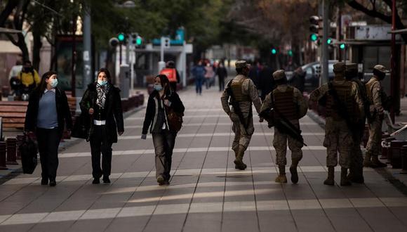 Tres mujeres caminan junto a un grupo de militares que patrullan durante la cuarentena obligatoria decretada para frenar el avance del coronavirus COVID-19 en Santiago (Chile). (EFE/Alberto Valdes).