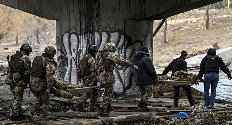 Militares de Ucrania llevan los cuerpos de sus camaradas en camillas en la ciudad de Irpin, al noroeste de Kiev, el 13 de marzo de 2022. (ARIS MESSINIS / AFP).