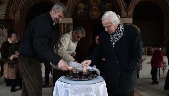 Fieles cristianos ortodoxos sumergen pan sagrado en una copa de vino tinto afuera de una iglesia en un monasterio en el pueblo de Milohori cerca de Ptolemaida al noroeste de Grecia. (Foto: Sakis MITROLIDIS / AFP)