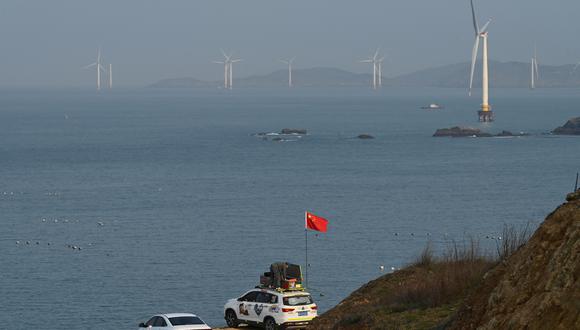Un hombre coloca una bandera china en su automóvil mientras se prepara para contemplar la vista del Estrecho de Taiwán, hacia la zona donde China dijo que realizaría ejercicios con fuego real al noreste de la isla de Pingtan, el punto más cercano de China a Taiwán, en China. La provincia sureste de Fujian el 10 de abril de 2023. (Foto de GREG BAKER / AFP)
