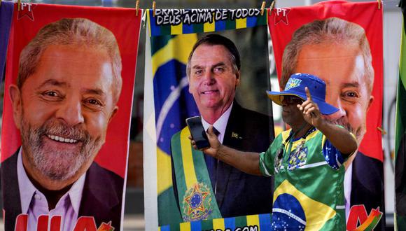 Un manifestante vestido con los colores de la bandera de Brasil camina frente a unas toallas de un vendedor ambulante que muestran a los candidatos presidenciales Lula da Silva y Jair Bolsonaro. (AP Foto/Eraldo Peres).