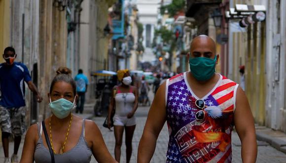 Un hombre vestido con una camiseta sin mangas con un diseño de la bandera de los EE.UU. y una máscara facial como medida preventiva contra la pandemia del nuevo coronavirus COVID-19, camina de la mano de una mujer en La Habana.