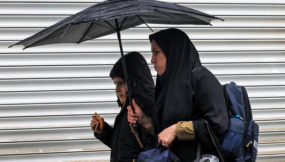 Una mujer y un niño caminan con un paraguas frente a una tienda cerrada en la plaza Enghelab en la capital de Irán, Teherán, el 5 de diciembre de 2022. (Foto de ATTA KENARE / AFP)