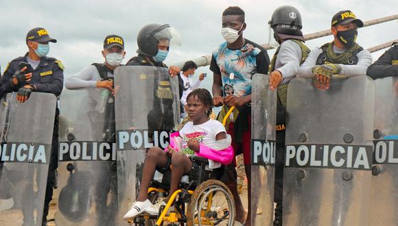 La policía abre paso a una mujer en silla de ruedas mientras una multitud de migrantes de varias nacionalidades, entre ellos haitianos, intentan cruzar al Perú por el Puente de la Amistad en la frontera con Brasil. (Foto: Radio Madre de Dios / AFP).