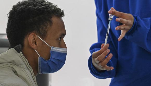 Un trabajador de salud muestra a un hombre un frasco de la vacuna CoronaVac de Sinovac Biotech contra el coronavirus en el estacionamiento del Aeropuerto Internacional El Dorado, en Bogotá (Colombia), el 16 de julio de 2021. (Foto de Juan BARRETO / AFP).