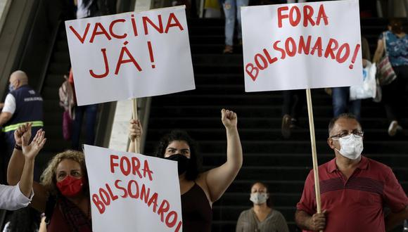 Manifestantes muestran carteles con las frases "¡Vacuna ya!" y "¡Fuera Bolsonaro" (en portugués) durante una protesta contra la gestión del presidente del país, Jair Bolsonaro, durante la pandemia del coronavirus, en una estación de autobús en Brasilia. (AP Foto/Eraldo Peres).