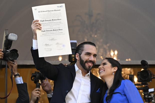 El presidente de El Salvador, Nayib Bukele, acompañado de su esposa Gabriela Rodríguez, muestra la certificación que lo acredita como mandatario electo para el período 2024 2029. (Foto de Marvin RECINOS / AFP).