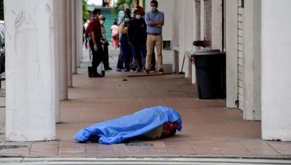 Las personas hacen cola frente a una tienda cerca del cadáver de un hombre en la ciudad de Guayaquil. Ecuador ha reportado 75 muertos por coronavirus. (REUTERS / Vicente Gaibor del Pino).