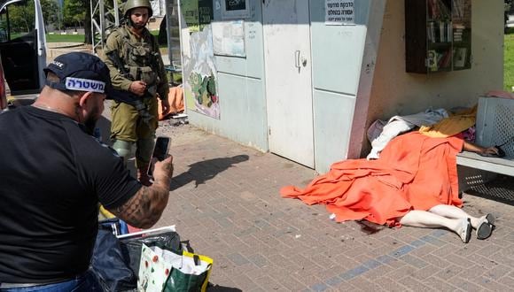 Un miembro de las fuerzas de seguridad israelíes toma una fotografía del cuerpo cubierto de un civil asesinado que yacía en la acera de la ciudad sureña de Sderot el 7 de octubre de 2023. (Foto de BAZ RATNER / AFP).