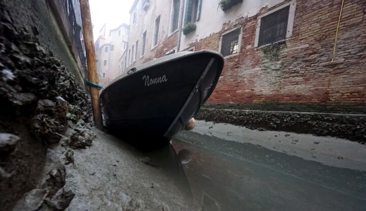 A small boat lies at the bottom of an internal canal at low tide in Venice, Italy.  (ANDREA MEROLA - EPA/ANSA).