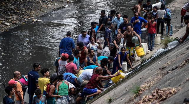 Decenas de caraqueños decidieron este lunes recoger agua del contaminado río Guaire debido a la imposibilidad de recibir agua en los hogares por causa del apagón que afecta a Venezuela. (AFP).