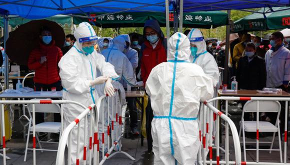 Trabajadores sanitarios arreglan su equipo mientras la gente se alinea para una prueba de COVID-19 este miércoles en Beijing, China.