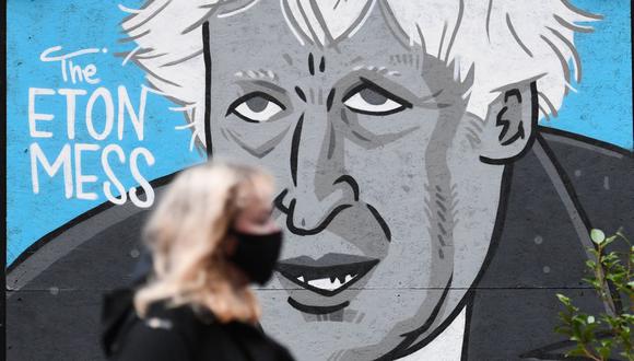 Una mujer que lleva una mascarilla debido a la pandemia de coronavirus pasa junto a un mural que representa al primer ministro británico, Boris Johnson en Manchester, Inglaterra. (Foto de Oli SCARFF / AFP).