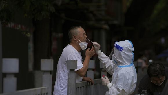 Un trabajador con traje protector toma un hisopo nasal de un hombre que ha estado en cuarentena domiciliaria como parte de los controles de COVID-19 en Beijing.