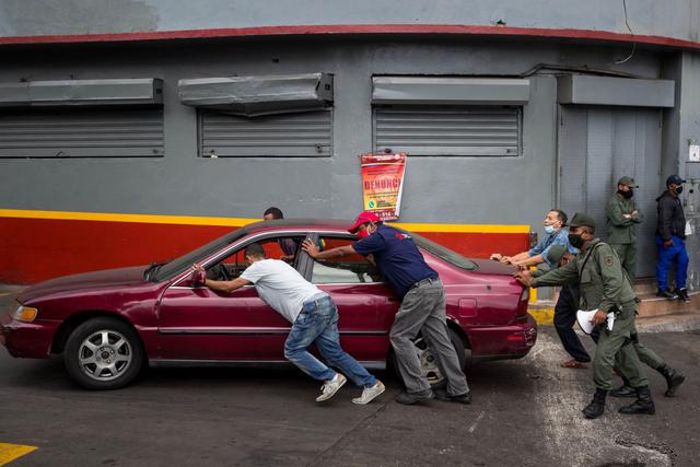Fotografía fechada el 18 de abril del 2020 donde se observa a un grupo de hombres y militares empujar un vehículo sin gasolina en Caracas, Venezuela. (Foto: EFE/ Miguel Gutiérrez)