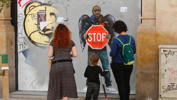 Una familia se detiene junto a una obra de arte del artista urbano italiano Salvatore Benintende, también conocido como "TVBOY", dedicada a George Floyd, en Barcelona. (AFP / PAU BARRENA)