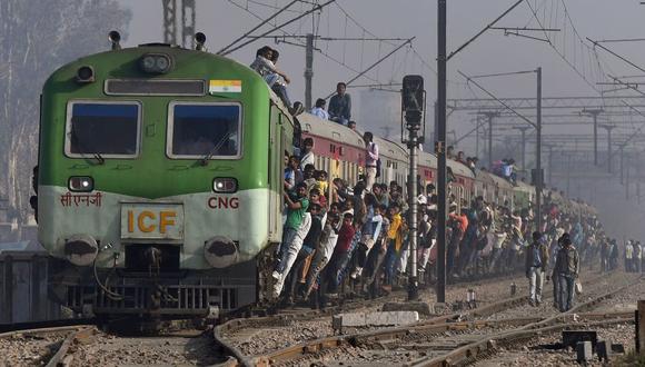 Los pasajeros se cuelgan de un tren cuando parte de una estación en las afueras de Nueva Delhi, India. (Foto: Prakash SINGH / AFP).