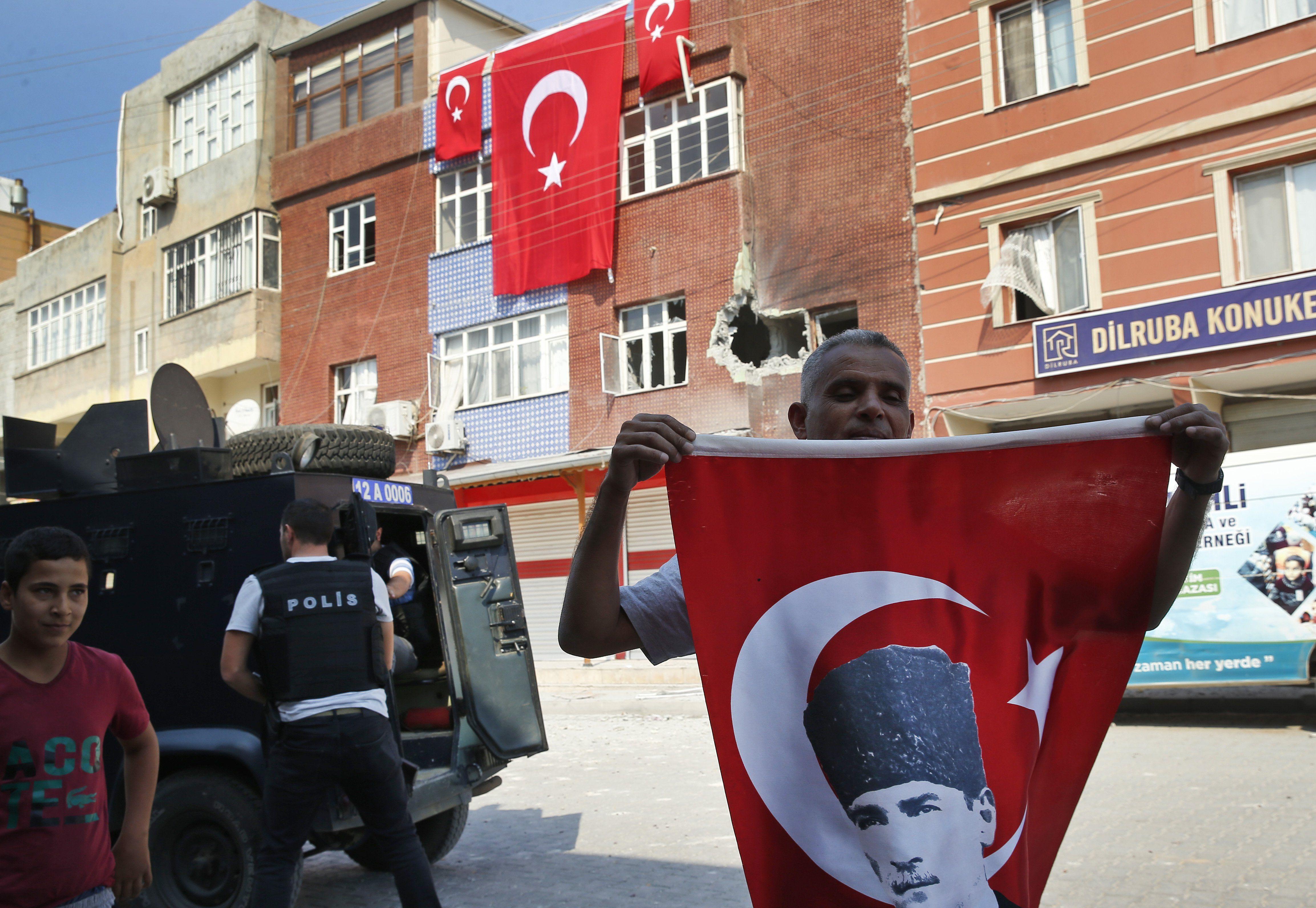 Un hombre con una bandera turca que lleva la imagen del fundador moderno de Turquía, Mustafa Kemal Ataturk, se encuentra frente a un edificio dañado por un mortero disparado desde Siria hacia la ciudad turca de Akcakale. (Foto AP / Lefteris Pitarakis).