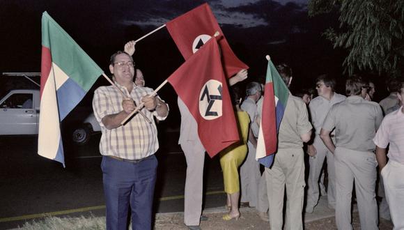Hombres ondean la bandera AWB del movimiento de extrema derecha durante la votación de los padres de una escuela sobre la participación de un atleta negro en una competencia deportiva, el 19 de febrero de 1987, en Pretoria, Sudáfrica. (TREVOR SAMSON / AFP).