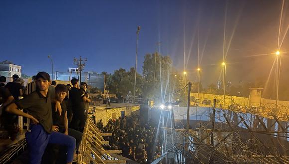 Manifestantes se paran en la parte superior de un edificio con vista a una calle llena de policías antidisturbios iraquíes que conducen a la embajada sueca en Bagdad el 20 de julio de 2023. (Foto de Ammar Karim / AFP)