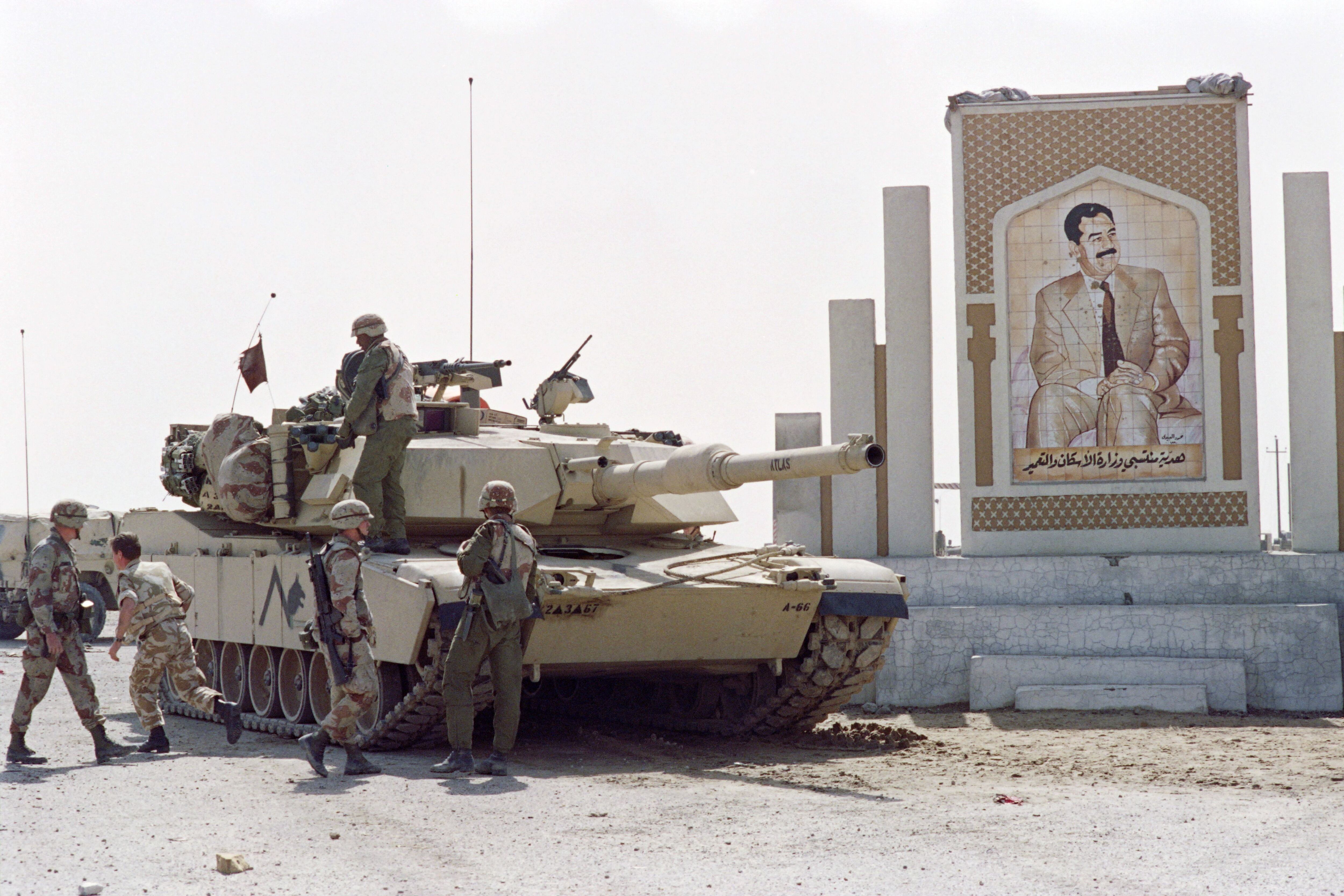 American soldiers stand next to an Abrams M1 A1 tank near a photograph of Iraqi President Saddam Hussein, on the outskirts of Kuwait City, March 1, 1991. (Photo by Pascal GUYOT/AFP).