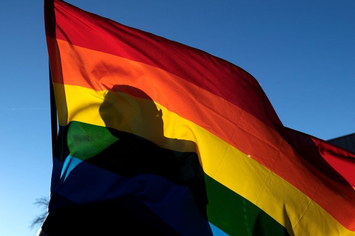 The silhouette of a member of the gay community is seen through a Pride flag as he pays his respects to the victims of the mass shooting at Club Q in Colorado, USA.  (JASON CONNOLLY / AFP).