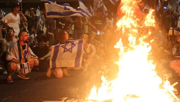 Manifestantes ondean banderas israelíes mientras se reúnen junto a una hoguera durante una protesta contra el proyecto de ley de reforma judicial del gobierno israelí en Tel Aviv el 18 de julio de 2023. (Foto de JACK GUEZ / AFP)