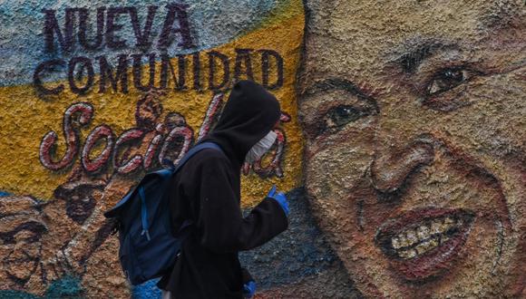 Un hombre con máscaras protectoras y guantes pasa junto a un mural que representa al fallecido presidente de Venezuela, Hugo Chávez, en el barrio de La Vega en Caracas. (Foto: Federico PARRA / AFP)