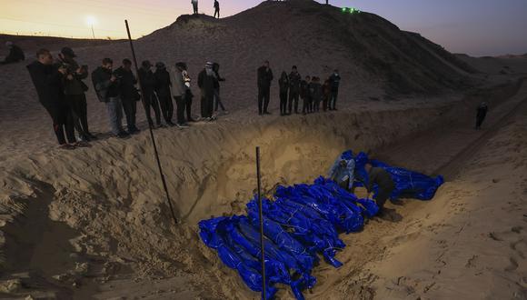 Gente observa cómo los cuerpos amortajados de los palestinos asesinados en el norte de Gaza son enterrados en una fosa común en Rafah, en el sur de la Franja de Gaza, el 26 de diciembre de 2023. (Foto de Mahmud HAMS / AFP)