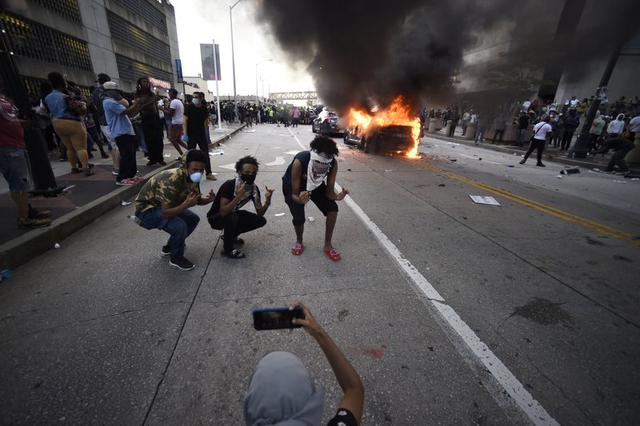 Un carro del Departamento de Policía de Atlanta arde mientras tres personas posan para una fotografía durante una manifestación contra la violencia policial. (AP Foto/Mike Stewart).