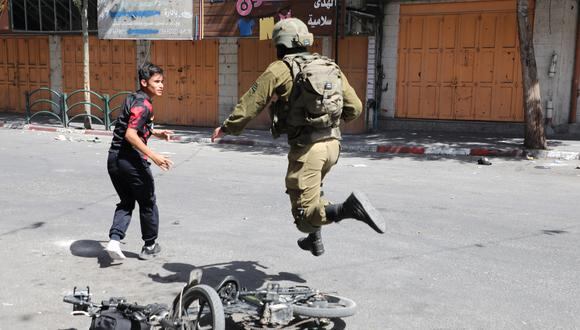 Un soldado israelí corre tras un joven palestino durante los enfrentamientos en el área de Bab al-Zawiya en el centro de la ciudad de Hebrón en la Cisjordania ocupada el 29 de septiembre de 2022. (Foto de MOSAB SHAWER / AFP)