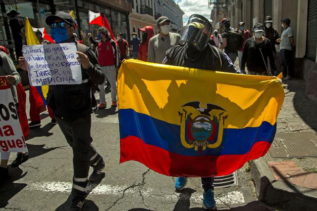 Un manifestante sostiene una bandera ecuatoriana mientras otra sostiene un cartel que dice "Si las guerras ahora son biológicas, es hora de disolver el ejército e invertir en medicina" durante una demostración contra los salarios más bajos y los recortes presupuestarios impuestos por el gobierno en medio de la nueva pandemia de coronavirus. en el centro de Quito, el 25 de mayo de 2020. (AFP / Cristina Vega Rhor).