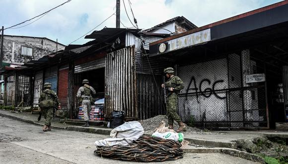 Soldados colombianos fotografiados junto a un grafiti de las AGC Autodefensas Gaitanistas de Colombia o paramilitares del Clan del Golfo en el pueblo de La Colonia en la región del bajo río Calima, cerca de la ciudad portuaria de Buenaventura, departamento del Valle del Cauca, el 18 de mayo de 2019. 2022. (Foto por JOAQUIN SARMIENTO / AFP)