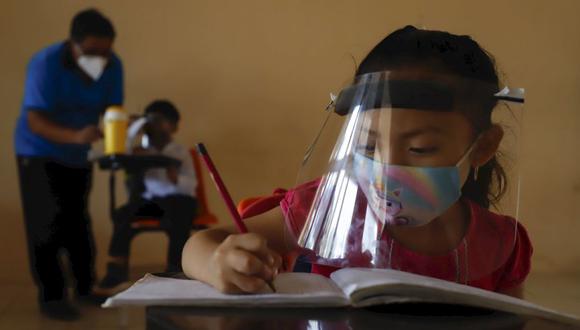 Con máscara y careta para frenar la propagación del nuevo coronavirus, Jade Chan Puc, de 10 años, escribe en su cuaderno durante el primer día de clases en la Escuela Primaria Indígena Valentín Gómez Farías en Montebello, Hecelchakán, estado de Campeche. (Foto: AP / Martin Zetina)