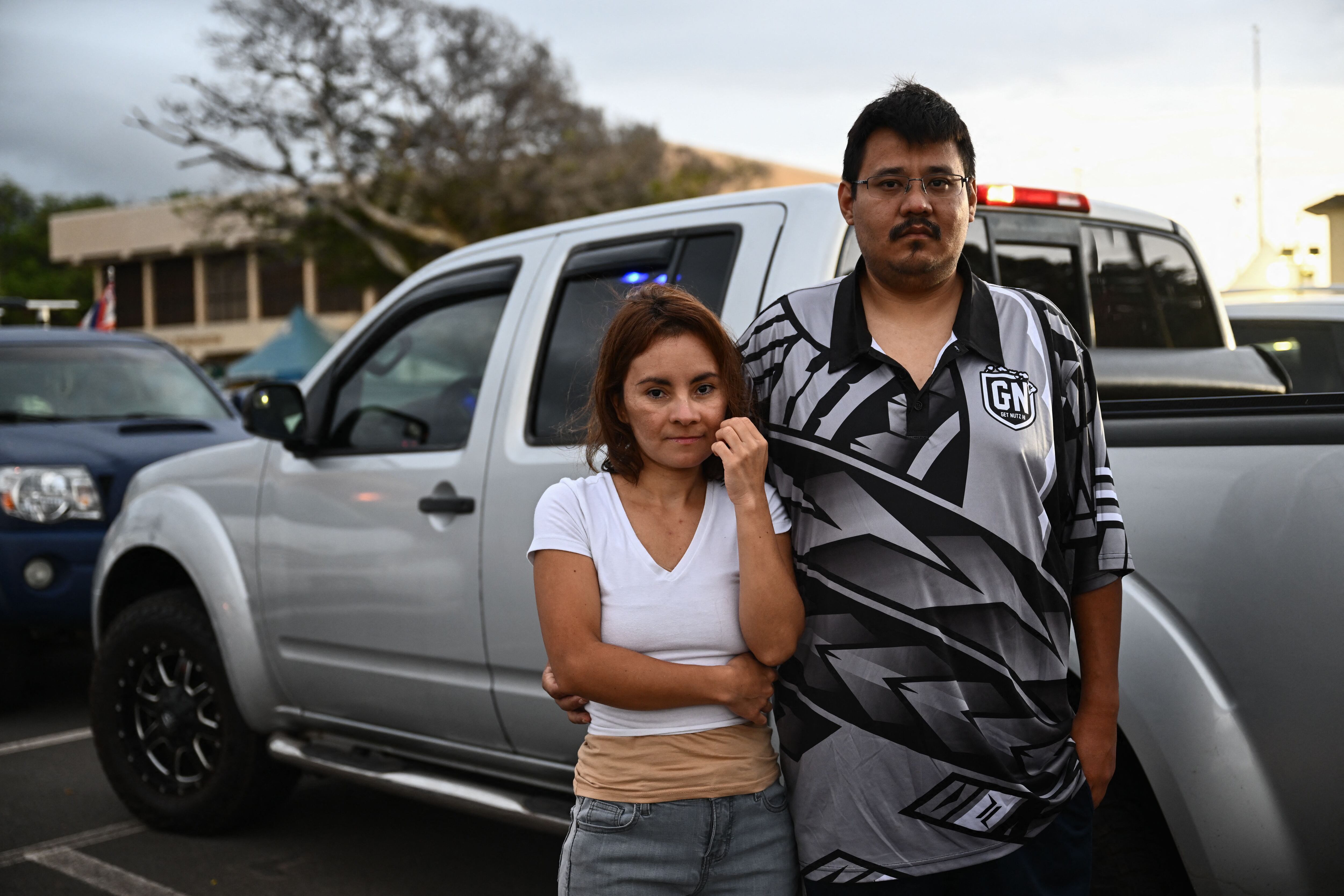Jose Victoria (R) and his wife Jennifer Herrera (L) pose for a portrait outside a shelter at War Memorial Stadium after fleeing their home near Lahaina after the West Maui wildfires in Wailuku, Hawaii.  (Photo by Patrick T. Fallon / AFP)