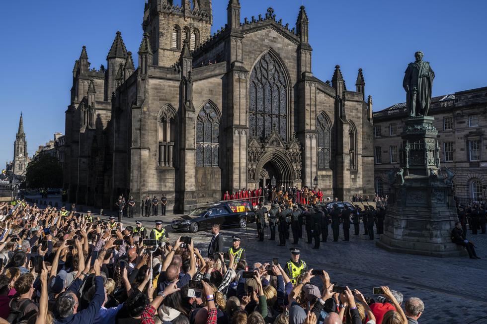 La gente toma fotos con sus teléfonos móviles mientras el cortejo fúnebre con el carro que lleva el ataúd de la reina Isabel sale de la catedral de St Giles en ruta al aeropuerto de Edimburgo. (AP/Bernat Armangue)