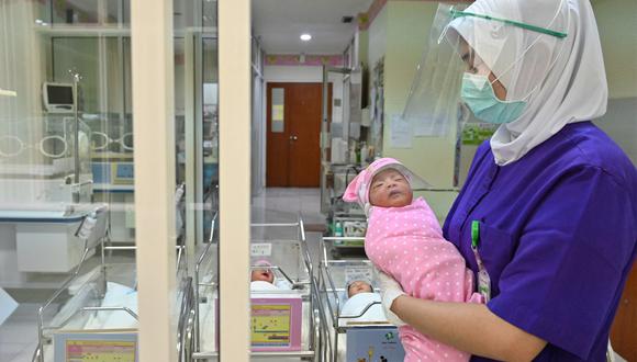 A nurse holds a newborn baby, seen wearing a face shield as a protective measure amid the COVID-19 coronavirus pandemic, at a maternity facility in Jakarta on April 21, 2020. (Photo by ADEK BERRY / AFP)