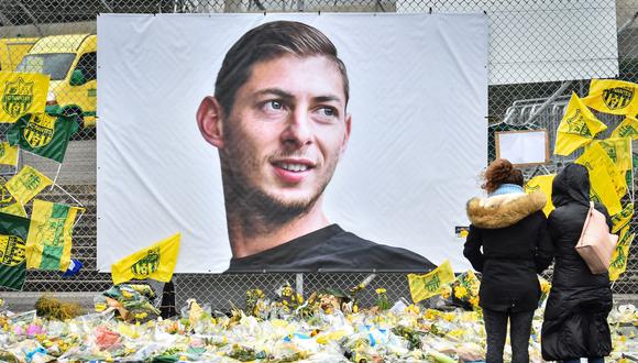 La gente mira las flores amarillas que se exhiben frente al retrato del delantero argentino Emiliano Sala en el estadio Beauvoir en Nantes, el 8 de febrero de 2019. (LOIC VENANCE / AFP).