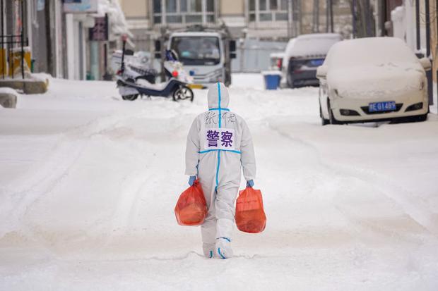 A policeman wearing a special protective suit carries groceries to distribute to Manzhouli residents, who have also been quarantined due to the omicron outbreak.  (Photo by AFP)