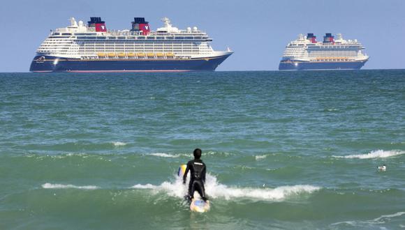 En esta fotografía de archivo del 24 de marzo de 2021, un surfista observa los barcos "Fantasy", a la izquierda y "Dream" de "Disney Cruise Line" mientras permanecen inmóviles frente a Cocoa Beach, Florida (Estados Unidos). (Joe Burbank/Orlando Sentinel/AP).