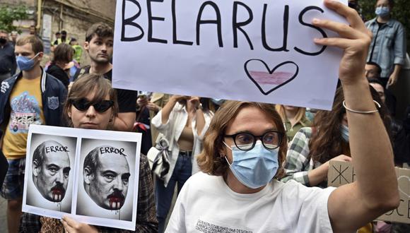Un miembro de la oposición en Bielorrusia sostiene un cartel que representa a Alexander Lukashenko con sangre en la boca y bigote junto a otro con un cartel que dice "#Bielorrusia libre", mientras participan con otros en una manifestación contra el gobierno. (Foto de Sergei SUPINSKY / AFP)