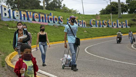 Personas que usan mascarillas para protegerse del coronavirus caminan por una autopista donde hay un letrero que dice "Bienvenidos a San Cristóbal", Táchira, en la frontera entre Venezuela y Colombia. (Foto de CARLOS EDUARDO RAMIREZ / AFP).