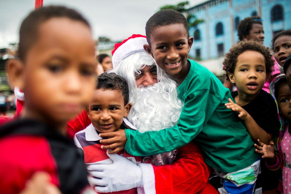 Un hombre disfrazado de Papá Noel abraza a niños durante una distribución de comida navideña organizada por la ONG Central  nica das Favelas (CUFA) en el barrio de chabolas del Complejo Penha, comúnmente conocido como Complejo Alemao, en Río de Janeiro, Brasil. (DANIEL RAMALHO / AFP)