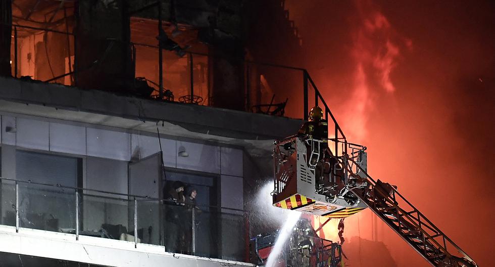 Dos residentes se encuentran en un balcón, antes de ser rescatados, mientras los bomberos luchan contra un gran incendio que arrasa un bloque residencial de varios pisos en Valencia el 22 de febrero de 2024. (Foto de José Jordán / AFP)