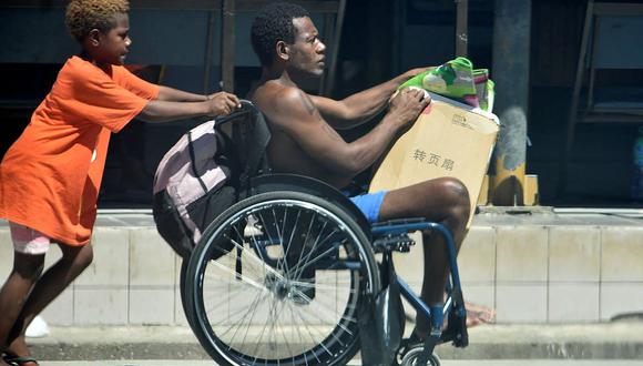 Un niño empuja la silla de ruedas de un familiar en el centro de Honiara, Islas Salomón, mientras la gente salía corriendo de sus oficinas y huía a terrenos más altos después de un fuerte terremoto. (Mavis PODOKOLO / AFP).