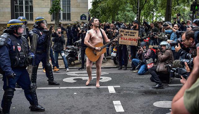 TOPSHOT - A naked man playing guitar stands in front of police officers during a protest called by several French unions against the labour law reform in Paris, on September 12, 2017. French unions launched a day of strikes and protests today against French President's flagship labour reforms, a key test as he stakes his presidency on overhauling the sluggish economy. More than 180 street protests are planned nationwide against the reforms, which are intended to tackle stubbornly high unemployment by loosening the rules that govern how businesses hire and fire people.
 / AFP / CHRISTOPHE ARCHAMBAULT