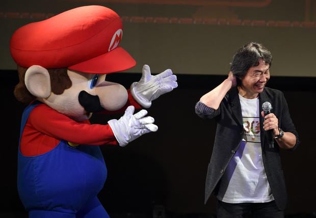 Nintendo game creator Shigeru Miyamoto reacts while standing with his character "Super Mario" during a live performance of the best-known Mario music to mark the game